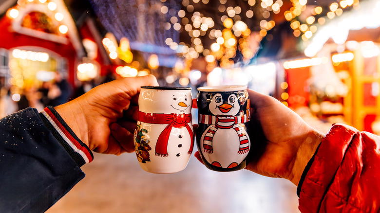 Two people holding up Christmas mugs against a market in the background