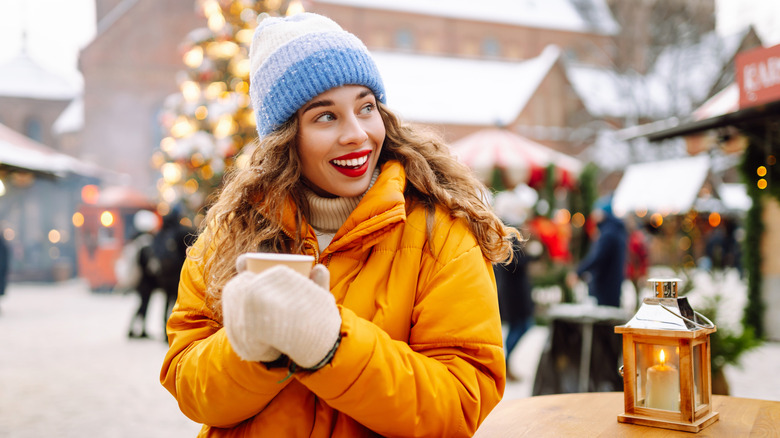 Woman at a Christmas market, dressed in warm cloths and holding Hot chocolate