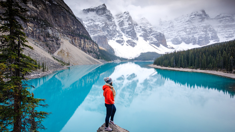 A woman standing above a turquoise lake with the Rocky Mountains in the background, Banff NP.