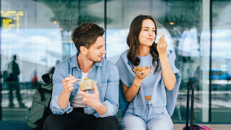 Two people eating snacks while seated in an airport terminal