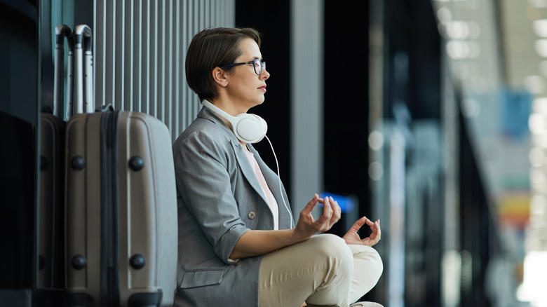 Woman meditating next to suitcase at airport