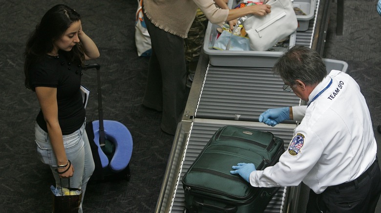 A frustrated passenger watches TSA agent open luggage