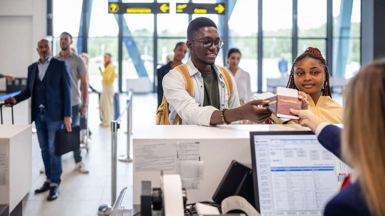 Two people handing over passports at airport check-in counter