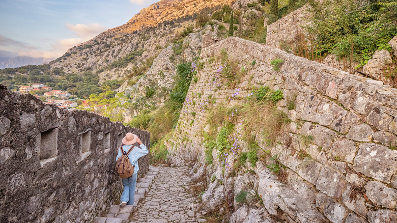 Woman with hat walking along stone staircase and framed by stone walls and mountains