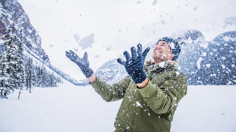 A man playing in the snow next to mountains and trees