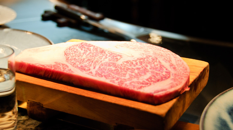 A highly-marbled Kobe beef steak sits uncooked on a wooden surface