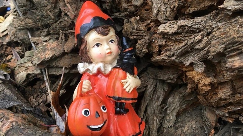 A small doll in a red dress and hat holding a pumpkin bag on the Witches' Tree