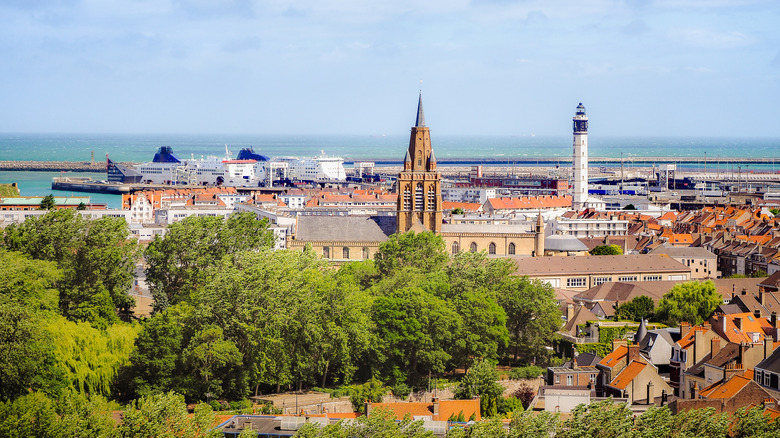 Trees and red roofs with church and lighthouse in center and sea in background