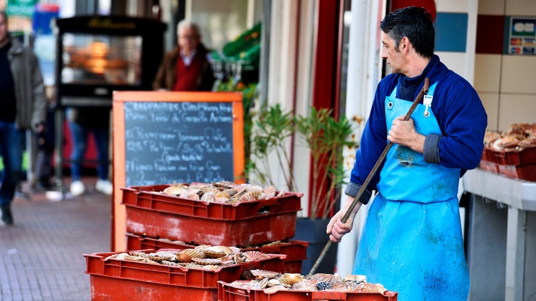 Man in apron selling scallops from crates in local market