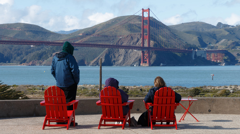 People sit in Adirondack chairs overlooking Golden Gate