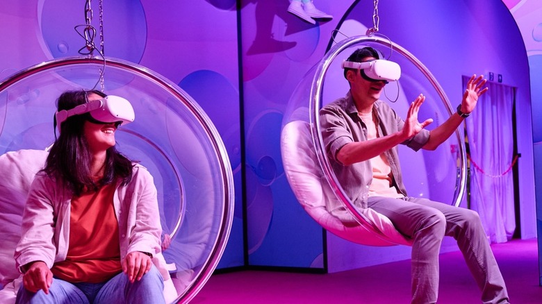 Two people with virtual reality goggles on and sitting in a swing chair