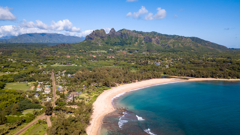 Aerial view of Anahola Beach Park with roads, buildings, mountains, and the shoreline in the distance.