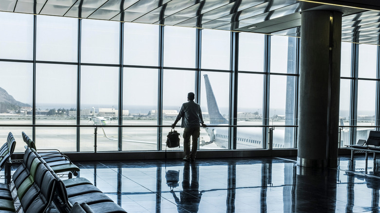 Man standing at an airport window watching the planes