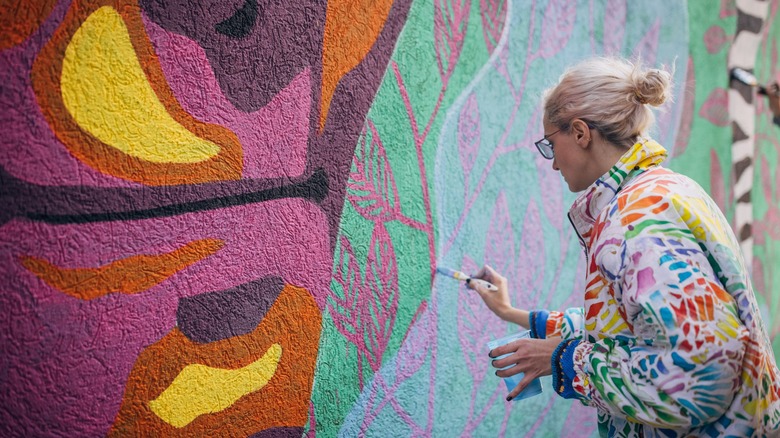 young woman painting bold pink, orange, yellow, green mural