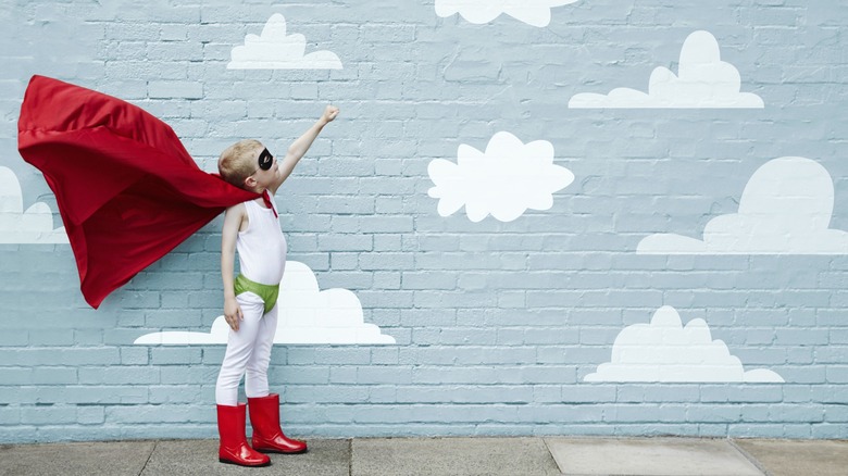 mural wall of white clouds on blue background with child in floating superhero costume pumping his fist