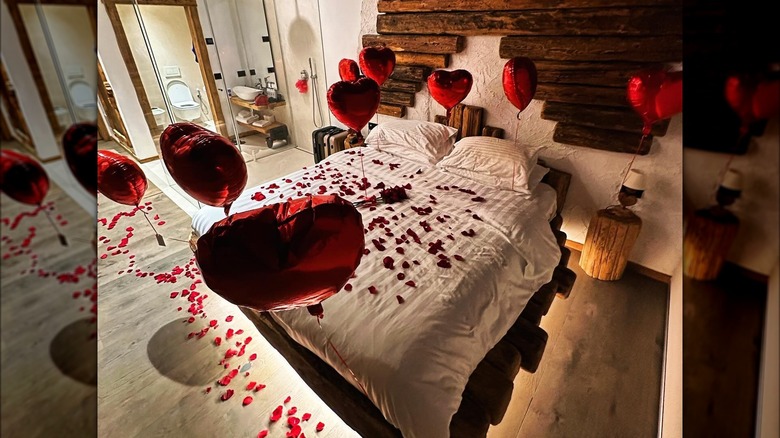 A bed at Chalet al Foss with red rose pedals and red heart balloons