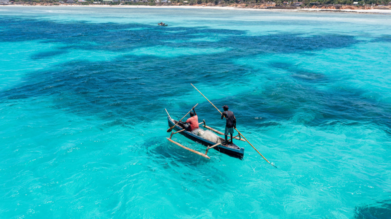 Two people manuever a traditional boat off the coastline of Mozambique