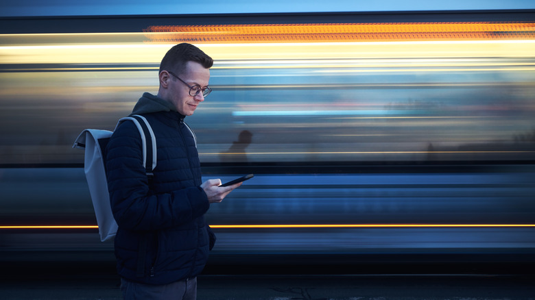 Commuting man looking at his phone as public transit blurs past in background