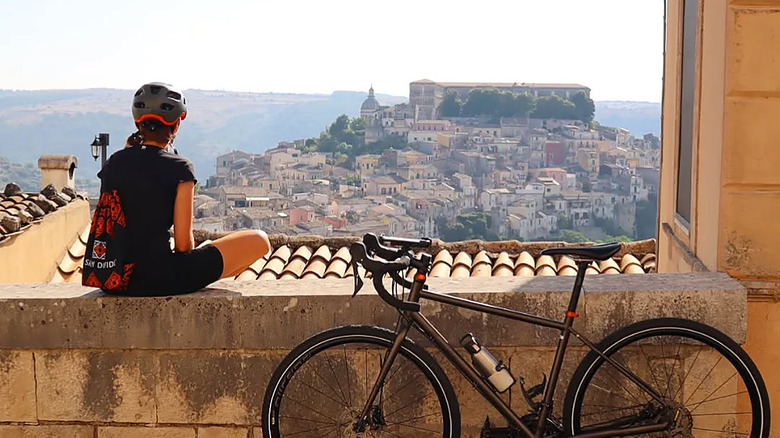 Woman looking at a beautiful Sicilian village from a terrace with her bike beside her