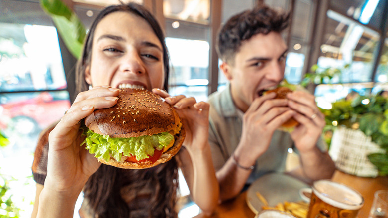 Two people eating burgers with beer in front of them