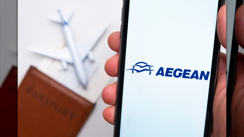 Hand holds phone with Aegean app with passport and toy plane in background