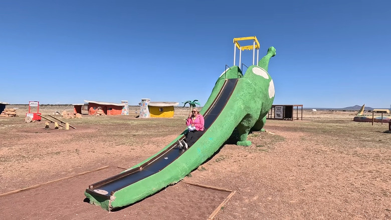 A woman slides down a green dino slide at Bedrock City