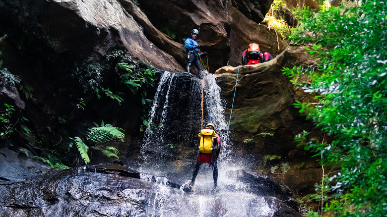 Person abseiling a waterfall with guides.