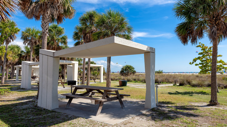 Picnic areas on green grass in front of Siesta Beach, Florida with cement covers and wooden benches