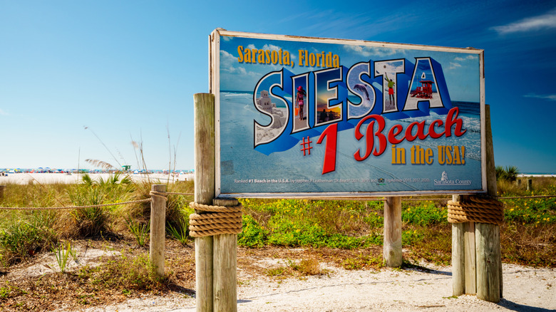 A sign in front of the beach reading "Sarasota, Florida, Siesta #1 Beach in the USA"