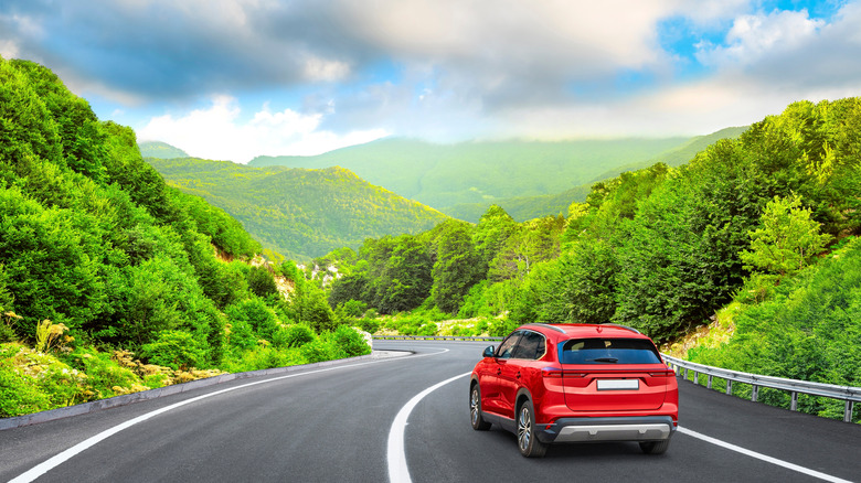 Red SUV driving on the highway through a green springtime landscape