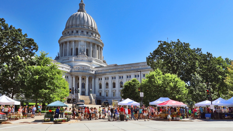 Dale County Farmers' Market vendors and customers in front of trees and the Wisconsin State Capitol building