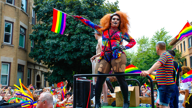 A drag queen holding a Pride flag on a float