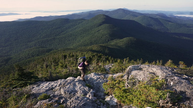 Hiker climbs along rocky trail surrounded by green mountains