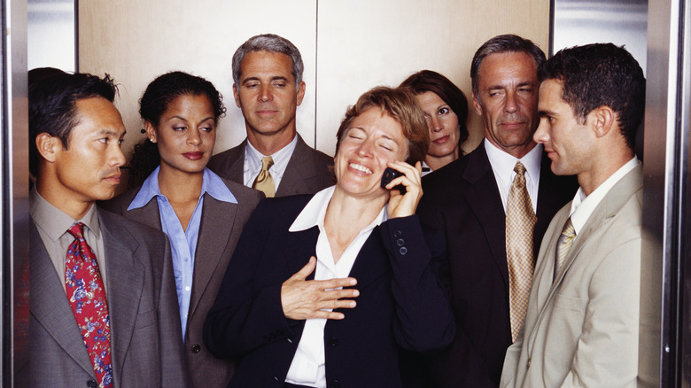 Person laughing on phone while surrounded by others in elevator