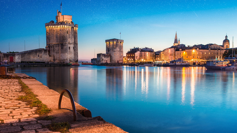 Twilight at historic port in France with stone towers and old city reflected in water