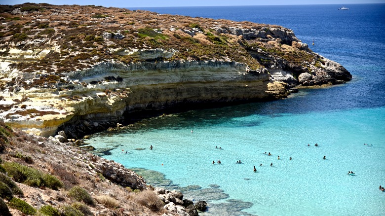 People swimming in a turquoise inlet in Lampedusa, Italy