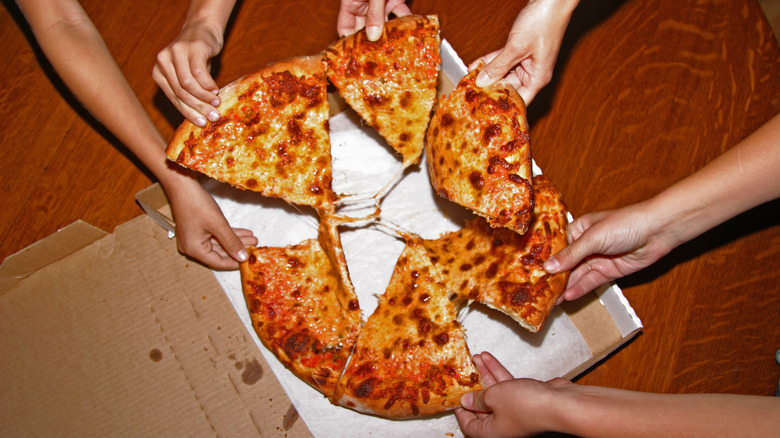 Hands grabbing at a pizza pie