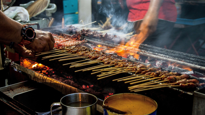 Grilling satay meat skewers with peanut sauce