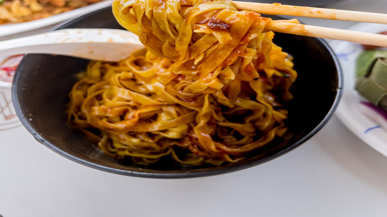 Chopsticks holding noodles with other Singapore dishes