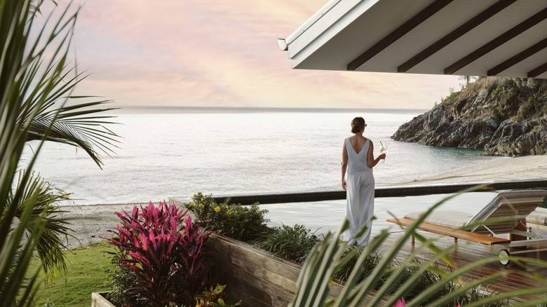 A woman stands with a drink outside one of the King Suites at Pelorus Private Island in Queensland, Australia, during sunset