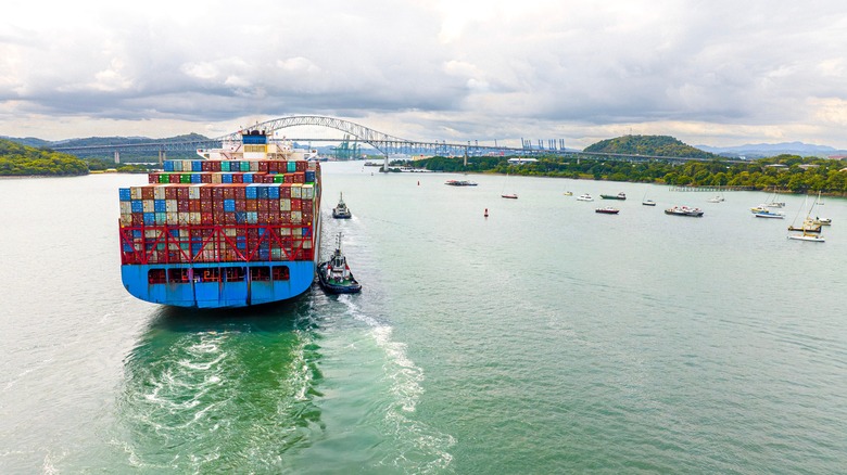 A cargo ship and small boats with a bridge in the background