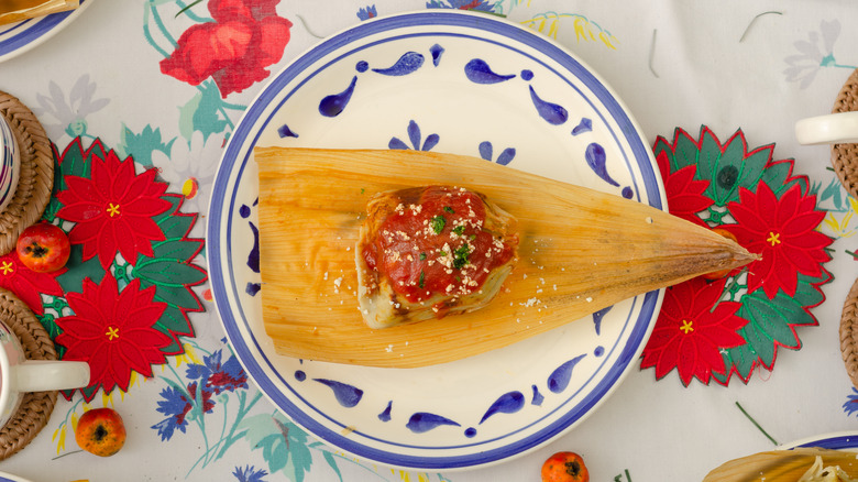 tamale with red sauce displayed on a tablecloth of Christmas flowers