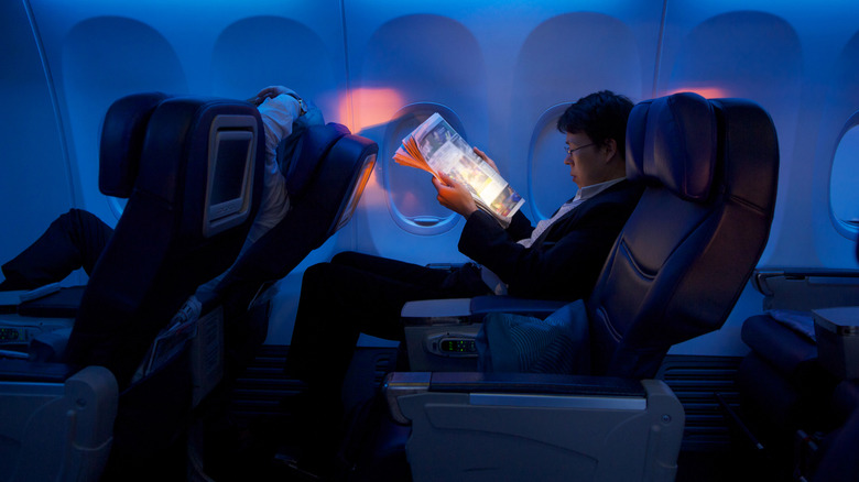 A man reading the newspaper in a premium economy airline seat