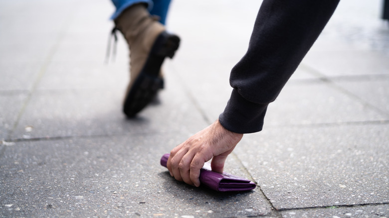 Someone picking up a dropped wallet on the sidewalk