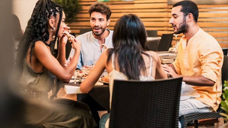 Men and women enjoying pizaa at a dinner table