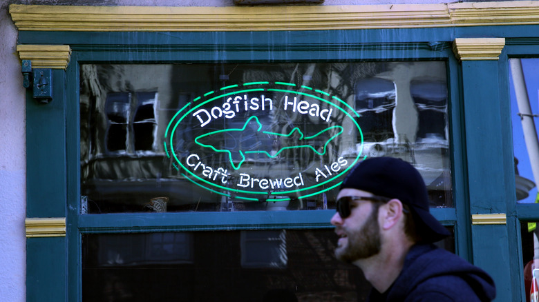 Man walking by Dogfish Head Brewery neon sign