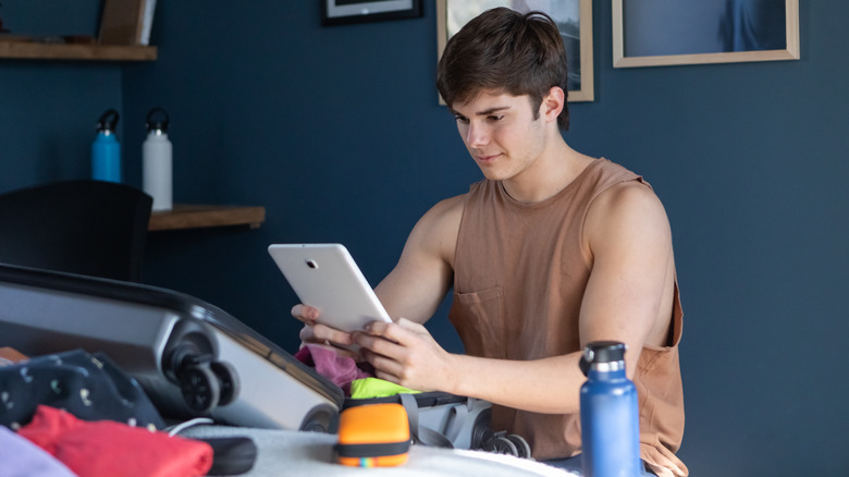 Young man looking at his tablet while packing