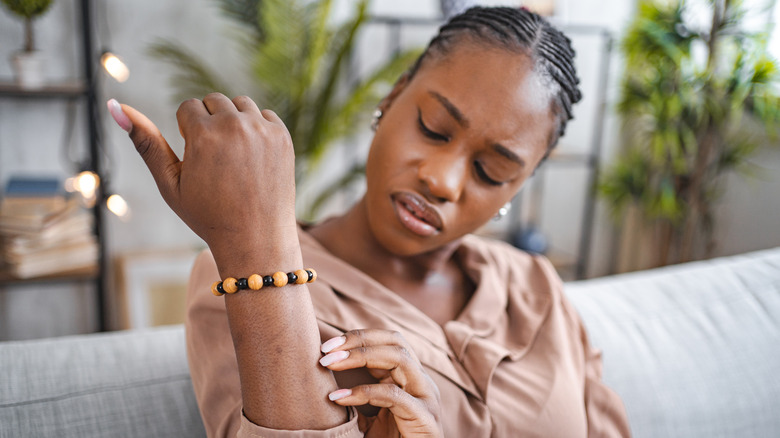 Woman sitting on a couch scratching an itch on her arm