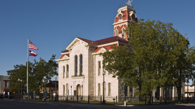 The red and white Lampasas County Courthouse with trees and the American flag