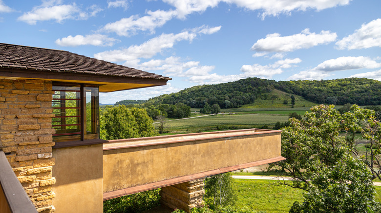 A stone house with a long walkway overlooking rolling green hills and woodland